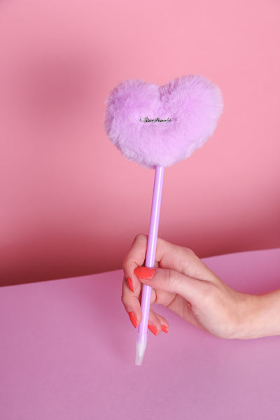 Stift mit Plüschherz auf dem ein silberner Metallaufnäher dran ist mit der Aufschrift: Cheerleader. in der Variante Lila. Der Stift wird von einer Hand mit orangefarbenem Nagellack gehalten. Der Untergrund ist Helllila und der Hintergrund rosa.