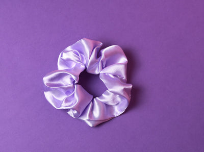 Ein lilafarbenes Scrunchie auf dunkel Lilanem Hintergrund.