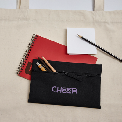 Cheer – Federetui in Schwarz mit Lila Aufschrift: Cheer. Das Etui hat einen Reißverschluss. Es liegt auf einem roten Block und Stifte chauen raus.