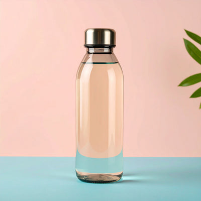 Eine durchsichtige Wasserflasche mit silbernem Deckel steht auf einem türkisem Papierhintergrund vor pastellrosafarbener Wand. Rechts gucken grüne Pflanzenbläter hervor.
