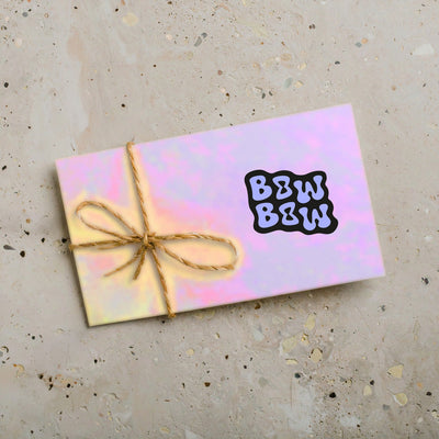 Geschenkgutschein auf Beton liegend. Auf dem bunten Gutschein ist eine Kordel und das Logo vom Bow Bow Cheer Shop.