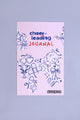 Cheerleading Journal liegt auf einem lila Hintergrund. Das Buch hat ein illustriertes Cover mit vielen Cheerleadingsymbolen.