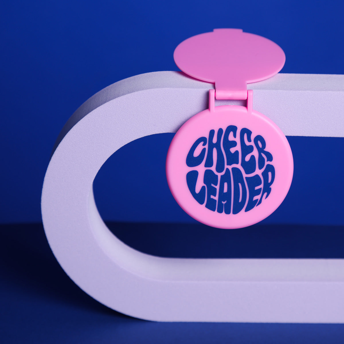 Cheerleader Handspiegel aufklappbar in Rosa zum Aufstellen auf blauem Hintergrund auf einem lilafarbenem Bogen  aufheklappt liegend