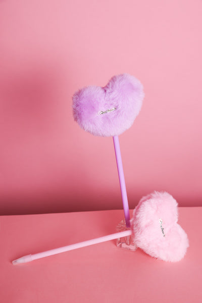 Stift mit Plüschherz auf dem ein silberner Metallaufnäher dran ist mit der Aufschrift: Cheerleader. Zwei Varianten: Rosa und Lila. Der lilafarbene Stift stehet hier in einem kleinen Glas-Stiftehalter auf rosafarbenem Hintergrund. Der rosafarbene Stift liegt daneben.