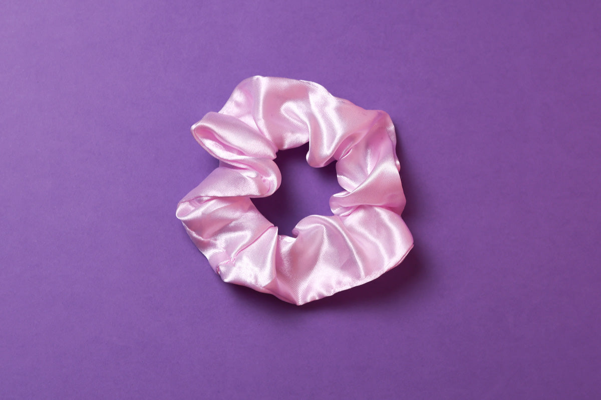 Ein hell lilafarbenes Scrunchie auf dunkel lilanem Hintergrund. 