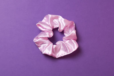 Ein hell lilafarbenes Scrunchie auf dunkel lilanem Hintergrund. 