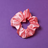 Ein corallefarbenes Scrunchie auf dunkel Lilanem Hintergrund. 