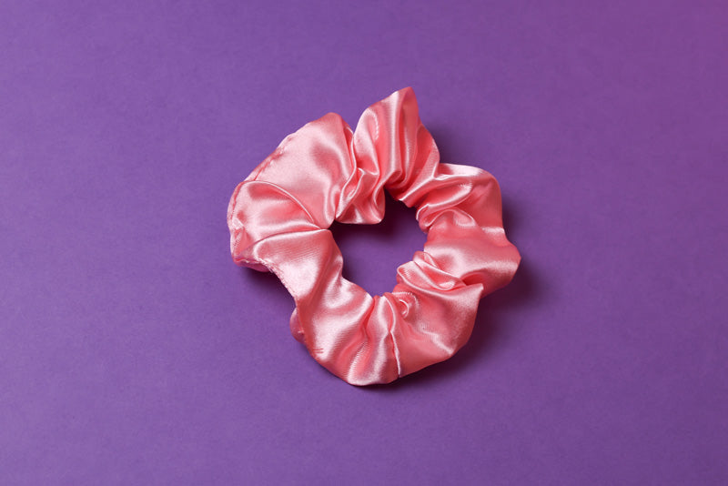 Ein corallefarbenes Scrunchie auf dunkel Lilanem Hintergrund. 