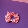 Ein corallefarbenes Scrunchie auf dunkel lilanem Untergrund und rosafarbenem Hintergrund.