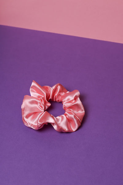 Ein corallefarbenes Scrunchie auf dunkel lilanem Untergrund und rosafarbenem Hintergrund.