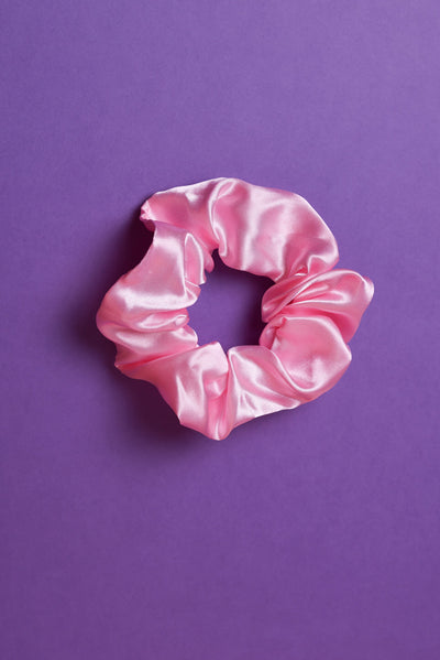 Ein rosafarbenes Scrunchie auf dunkel Lilanem Hintergrund. 