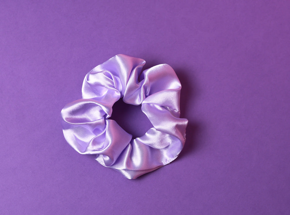 Ein lilafarbenes Scrunchie auf dunkel Lilanem Hintergrund. 