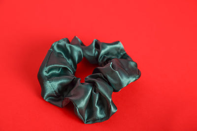 dunkel Grünes Satinhaargummi, auch Scrunchie genannt auf rotem Haargummi.