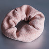Scrunchie aus Jacquardstoff mit einem geriffeltem dreidimensionalem Muster in altrosa liegt auf silbernem strukturiertem Untergrund.