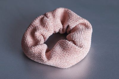 Scrunchie aus Jacquardstoff mit einem geriffeltem dreidimensionalem Muster in altrosa liegt auf silbernem strukturiertem Untergrund.