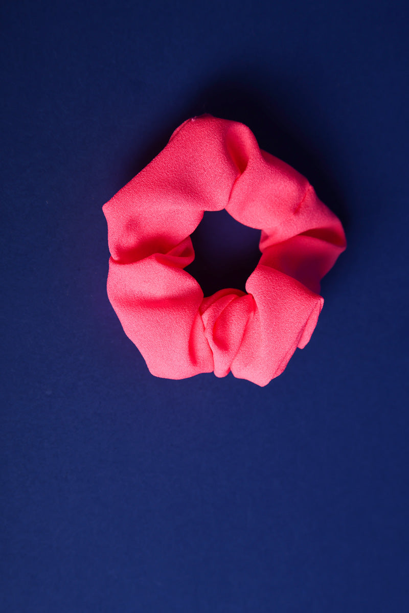 Scunchie aus Stoff in Neonpink auf blauem Hintergrund.