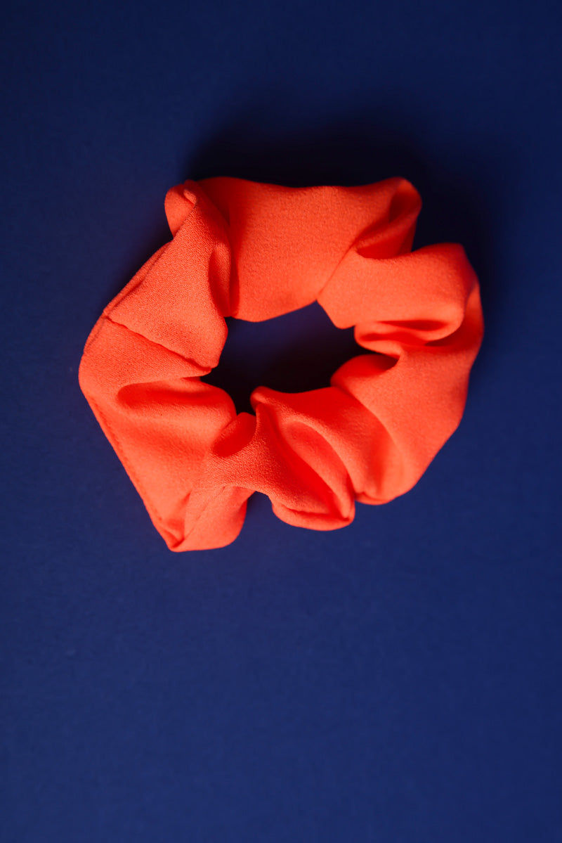 Scunchie aus Stoff in Neonorange auf blauem Hintergrund.