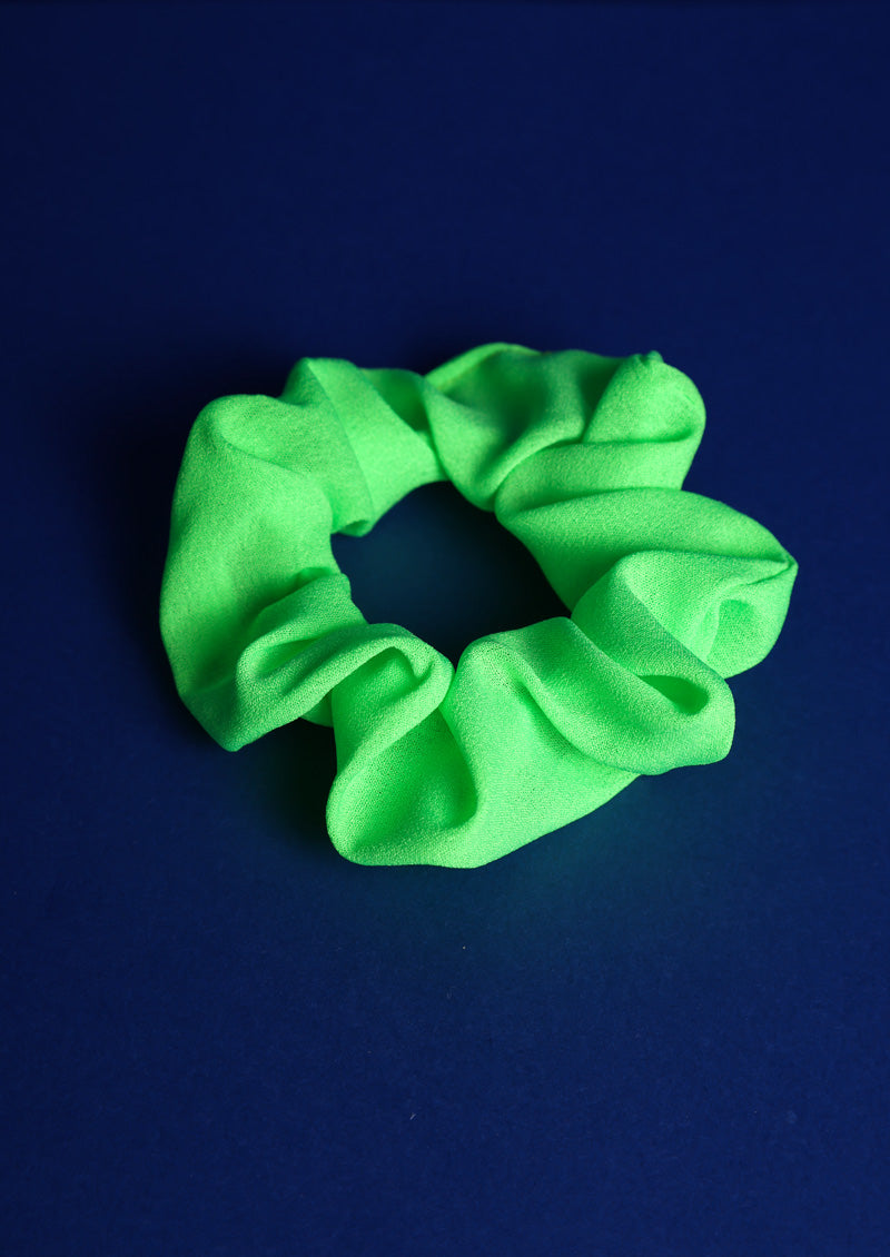 Scunchie aus Stoff in Neongrün auf blauem Hintergrund.