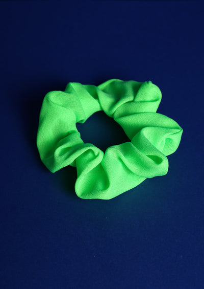 Scunchie aus Stoff in Neongrün auf blauem Hintergrund.
