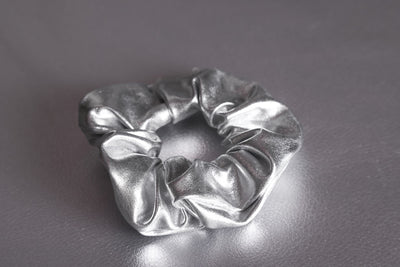 silber mattes Stoff-Haargummi, auch Scrunchie genannt, liegt auf silbernem Untergrund.