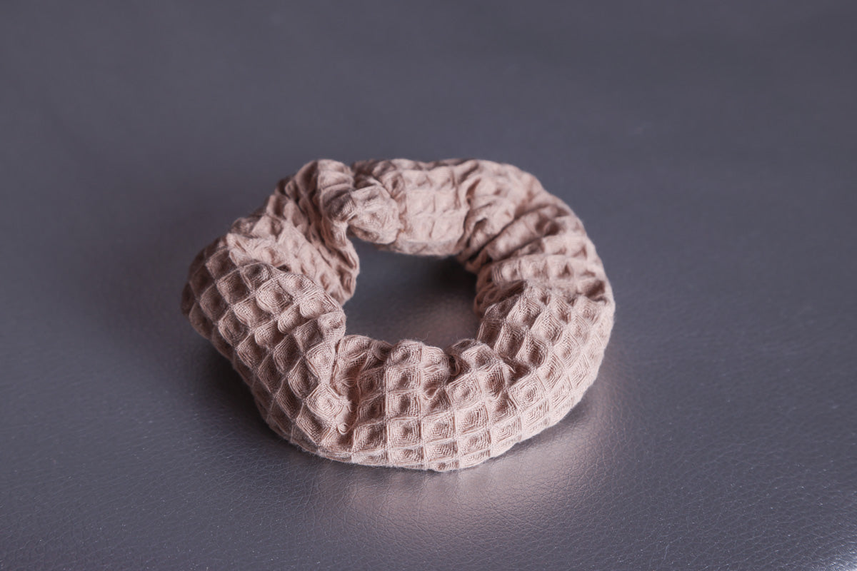 Scrunchie in Cappuccino Farbton mit 3-D Waffelmuster liegt auf silbernem, strukturiertem Hintergrund.