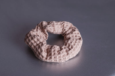 Scrunchie in Cappuccino Farbton mit 3-D Waffelmuster liegt auf silbernem, strukturiertem Hintergrund.