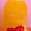rote, elastische Haargummis in rot, als Doppelpack, liegen auf einem gelben Acrylglasständer auf orangefarbenem Untergrund mit rosafarbenem Hintergrund.