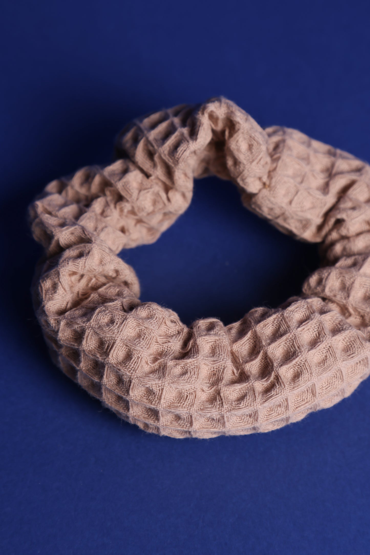 Scrunchie in Cappuccino Farbton mit 3-D Waffelmuster liegt auf blauem Hintergrund.