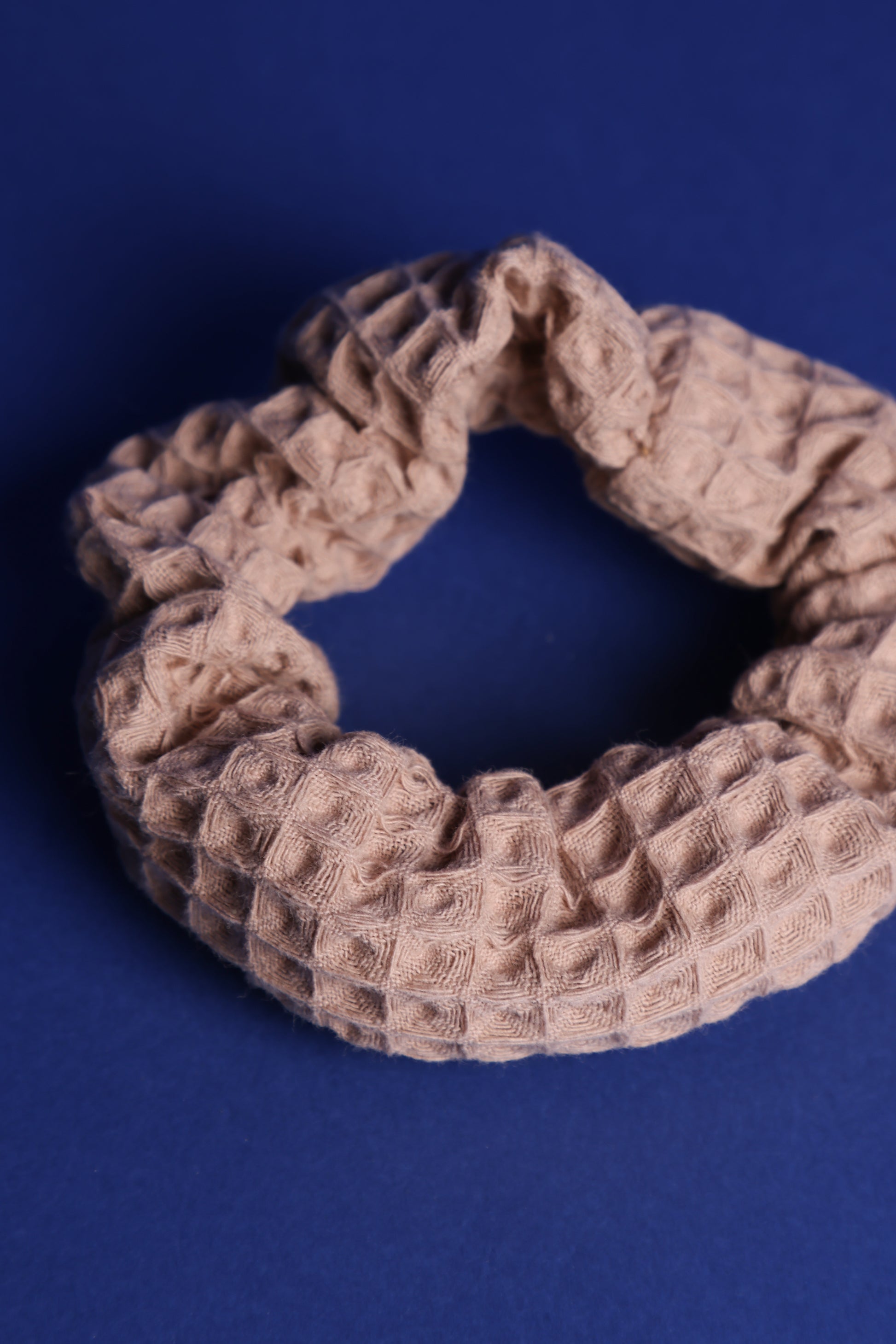 Scrunchie in Cappuccino Farbton mit 3-D Waffelmuster liegt auf blauem Hintergrund.