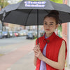 Mädchen mit roter Weste und lila Pullunder, dunklen Haaren im Dutt hält draußen einen schwarzen Regenschirm mit der Aufschrift: "CHEERLEADER" in Pixelart..
