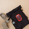 Cheer Roll Top Backpack in schwarz auf weißem Hintergrund. der Rucksack hat seitliche Gurt justierungen und Seitentaschen in einer ist eine Trinkflasch zu sehen. Auf dem Motiv ist eine weit offene Lippe mit Zähnen zu sehen. In der Öffnung vom Mund steht: Don't mess with my cheer squad please. Der Rucksack wurde auf beigem Hintergrund fotografiert. Neben dem Rucksack liegen Gartenlatschen mit Plateau.