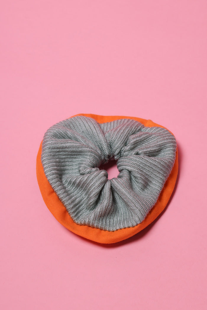 Mintfarbenes, gestricktes Wollscrunchie mit orangefarbenem Rand liegt auf rosafarbenem Hintergrund.