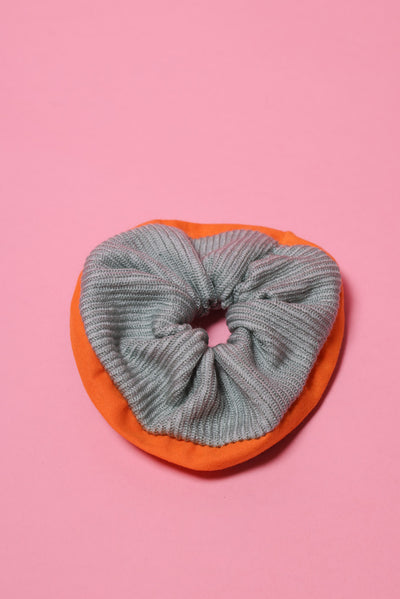 Mintfarbenes, gestricktes Wollscrunchie mit orangefarbenem Rand liegt auf rosafarbenem Hintergrund.