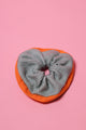 Mintfarbenes, gestricktes Wollscrunchie mit orangefarbenem Rand liegt auf rosafarbenem Hintergrund.