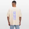 Eine dunkelhäuftige, weiblich gelesene Person mit einem lockigen Zopf trägt ein beiges Shirt mit dem Motiv: COUNT. Das Oversized Organic T-shirt hat die Farbe natural raw. Auf dem Shirt ist das Motiv: ready,set, 5,6,7 and 8,1,2,up zu sehen. Zudem trägt die Person eine Jeanshose und steht vor weißem Hintergrund.