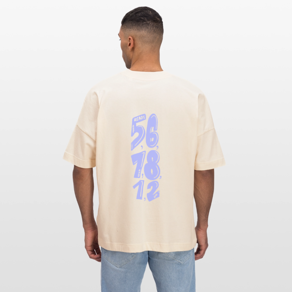 Eine dunkelhäuftige, weiblich gelesene Person mit einem lockigen Zopf trägt ein beiges Shirt mit dem Motiv: COUNT. Das Oversized Organic T-shirt hat die Farbe natural raw. Auf dem Shirt ist das Motiv: ready,set, 5,6,7 and 8,1,2,up zu sehen. Zudem trägt die Person eine Jeanshose und steht vor weißem Hintergrund.