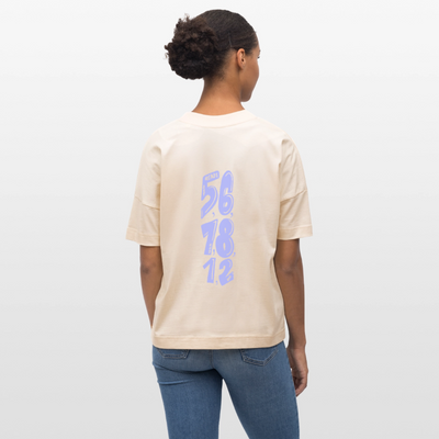 Eine dunkelhäuftige, weiblich gelesene Person mit einem lockigen Zopf trägt ein beiges Shirt mit dem Motiv: COUNT. Das Oversized Organic T-shirt hat die Farbe natural raw. Auf dem Shirt ist das Motiv: ready,set, 5,6,7 and 8,1,2,up zu sehen. Zudem trägt die Person eine Jeanshose und steht vor weißem Hintergrund.
