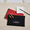 Cheer – Federetui in Schwarz mit Lila Aufschrift: Cheer. Das Etui hat einen Reißverschluss. Es liegt auf einem roten Block und Stifte chauen raus.