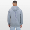 Ein mänlich gelesene Person trägt hier einen Hoodie mit dem Motiv: One Line Partnerstunt Scorpion in hellem blau. Die Person trägt eine Jeanshose und hat dunkle, kurze Haare. Sie steht vor einer weißen Wand.