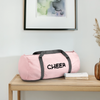 Sporttasche in rosa mit grauen Griffen und der Aufschrift Cheer.Die Tasche liegt iauf einem Holz-Sideboard. Die Tasche ist beidseitig bedruckt. Oben ist ein Bilderrahmen und seitlich im Rand steht eine Blumenvase in beige aus Glas.