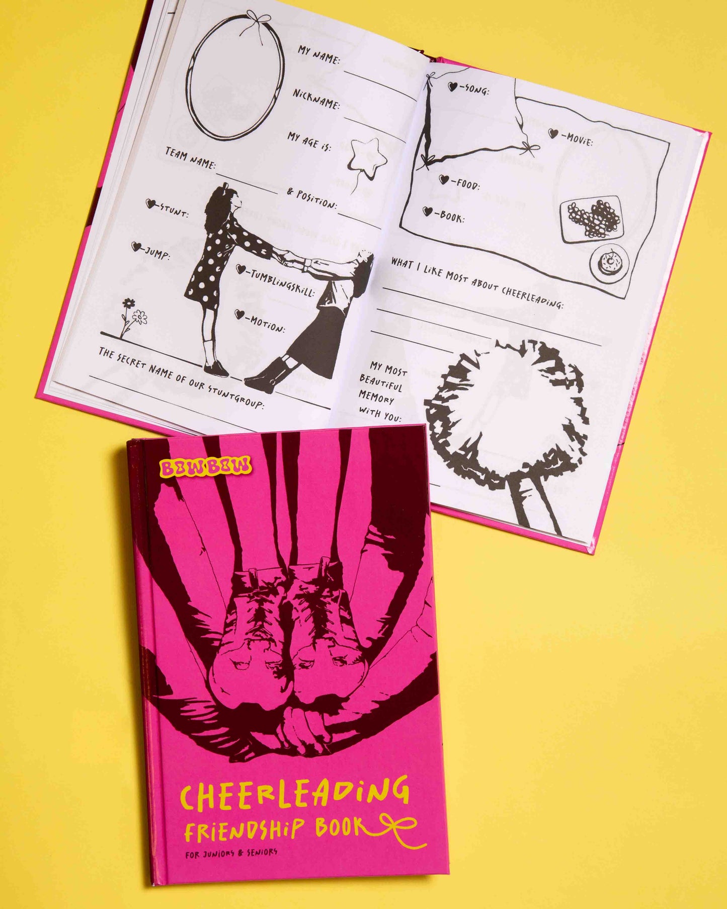 On yellow Background you see the book: CHEERLEADING FRIENDSHIP BOOK: for Juniors & Seniors. The Cover shows an illustration of arms showing a baskettoss with one person on the basketcross position. The Cover is Pink, yellow and Brown. The other book is open and shows the black and white design oft the book, that you can color.