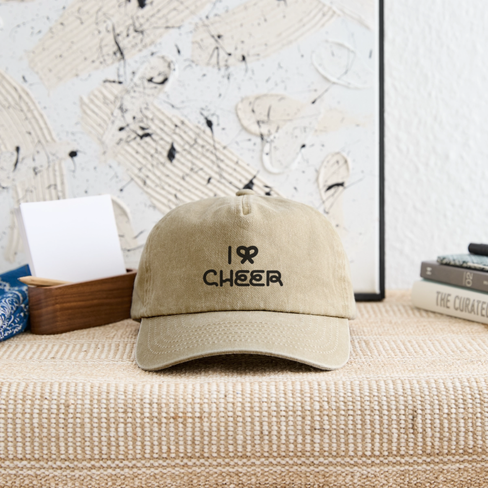 I BOW CHEER Vintage Cap in vintage beige lying on a beige Couch with Books and a Canvas with art in the background.