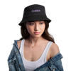 Zu sehen ist ein Bucket Hat in khaki/schwarz mit dem Aufdruck: I BOW (als Schleifensymbol) Cheer auf dem Kopf einer Frau. Sie hat braune Augen, helle Haus, dunkle Augenbrauen und Haare, rosa geschminkte Lippen, Creolen und eine Kette an. Sie trägt eine Jeansjacke und ein weißes Top.