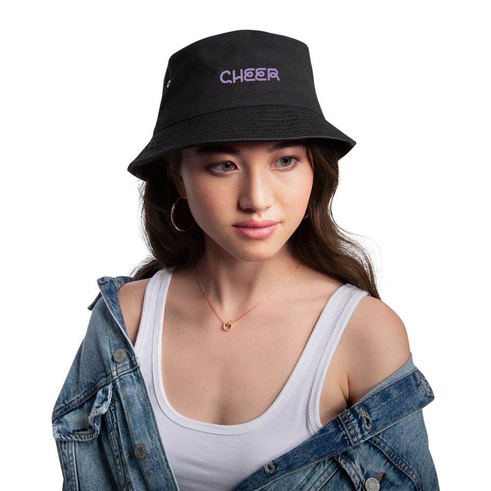 Zu sehen ist ein Bucket Hat in khaki/schwarz mit dem Aufdruck: I BOW (als Schleifensymbol) Cheer auf dem Kopf einer Frau. Sie hat braune Augen, helle Haus, dunkle Augenbrauen und Haare, rosa geschminkte Lippen, Creolen und eine Kette an. Sie trägt eine Jeansjacke und ein weißes Top.