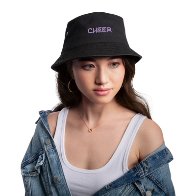 Zu sehen ist ein Bucket Hat in khaki/schwarz mit dem Aufdruck: I BOW (als Schleifensymbol) Cheer auf dem Kopf einer Frau. Sie hat braune Augen, helle Haus, dunkle Augenbrauen und Haare, rosa geschminkte Lippen, Creolen und eine Kette an. Sie trägt eine Jeansjacke und ein weißes Top.