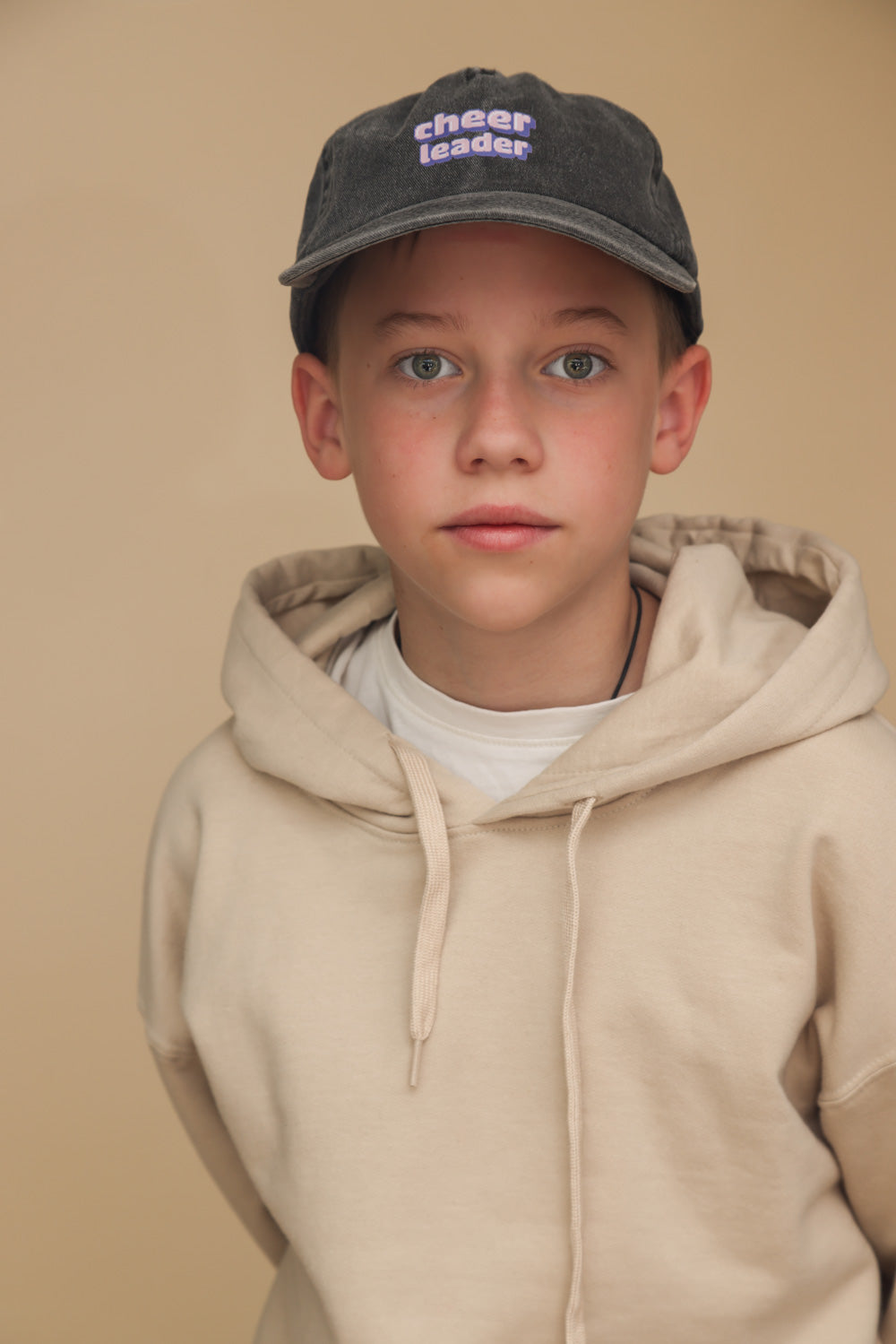 Zu sehen ist ein Cheerleader Pixelart Motiv auf einer Relaxed Vintage Cap in der Farbe vintage black. Diese wird getragen von einem Junior Jungen, der einen beigen Pullover trägt und vor beigem Hintergrund steht.