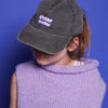 Zu sehen ist ein Cheerleader Pixelart Motiv auf einer Relaxed Vintage Cap in der Farbe vintage black ist hier auf dem Kopf von einem kleinen Mädchen zu sehen. Das Mädchen trägt einen lilafarbenen Pullunder und steht vor einem blauen Hintergrund. Das Gesicht ist bis auf die Lippen von der Cap versteckt.